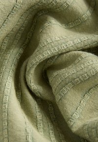 Soft, textured green fabric with woven accents and a raised geometric pattern, displaying gentle folds and a subtle sheen.