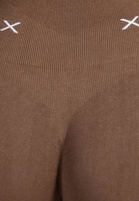 Leggings marrones con diseño acanalado y sin costuras. Presentan una pretina alta y detalles de costuras blancas en contraste. Textura suave.