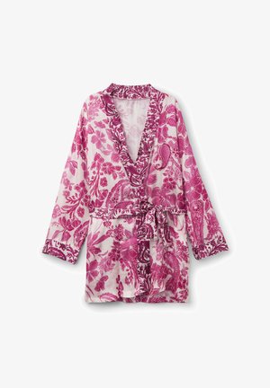 Robe à fleurs rose et blanche, manches longues, col châle, ceinture nouée à la taille, présentée sur un fond uni.