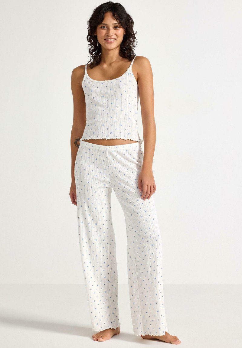 Vit ribbat pyjamaset med blått blommönster. T-shirten har tunna axelband och en scalloped fåll, medan byxorna är vida och också har en scalloped fåll.