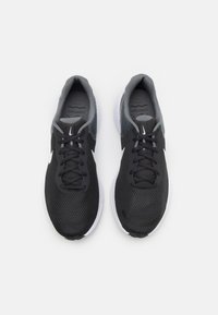 Des chaussures de sport noires et grises avec une tige en maille, un bout rond et un système de laçage. Elles présentent une semelle blanche et un détail du logo Nike.
