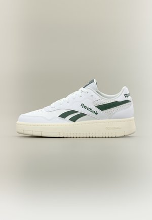 Άσπρο αθλητικό παπούτσι Reebok με σκούρα πράσινες πλευρικές ρίγες, μπεζ σόλα και λογότυπο Reebok στο πλάι και στη φτέρνα σε ουδέτερο φόντο.