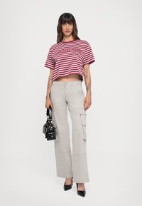 Kort rood-wit gestreept T-shirt met logo, gecombineerd met lichtbeige cargobroek met zakken, gedragen met zwarte hakken en handtas.