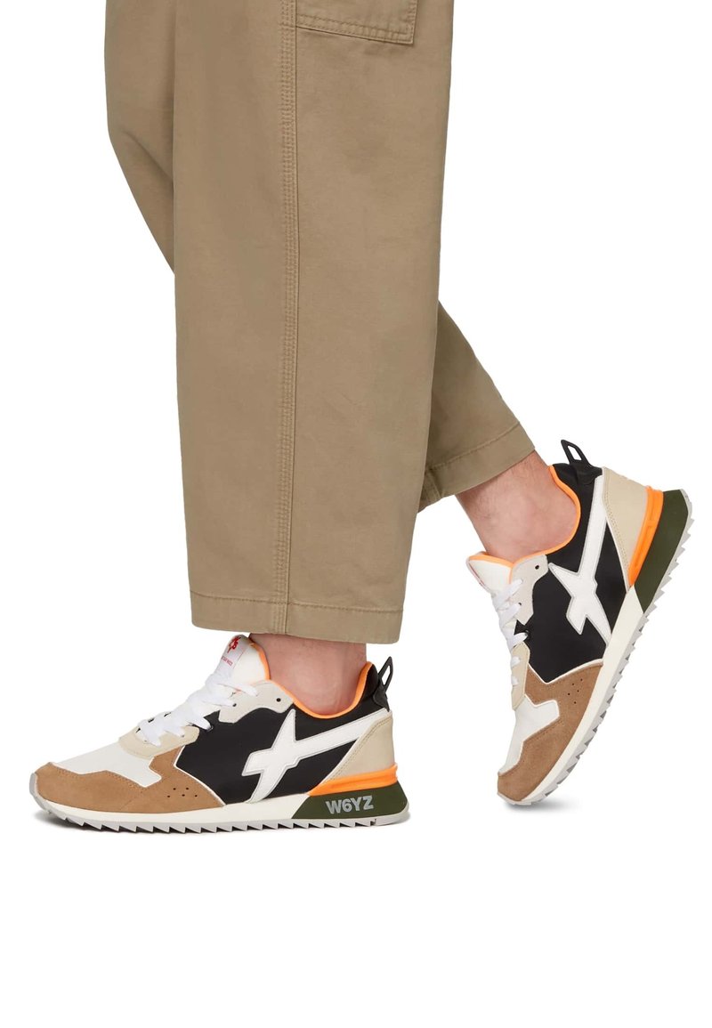 Sneakers z mixem czerni, bieli, beżu oraz pomarańczowych akcentów; posiadają teksturowane materiały, żebrowaną podeszwę oraz wyraźne logo po boku.