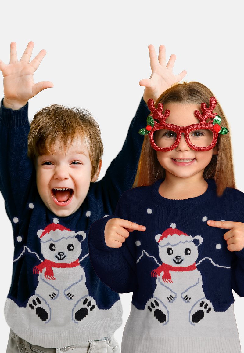 Due bambini con maglioni blu navy coordinati con orsi polari; la bambina indica il maglione e indossa occhiali rossi a forma di corna, il bambino alza le mani eccitato.