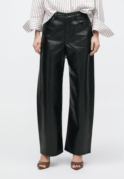 Musta nahast laia säärega püksid, millel on sile tekstuur, ees taskud ja nööpidega esikäepide, kombineeritud pruunide kontsakingadega.