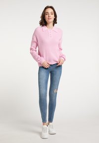 Różowy dziany sweter z kołnierzykiem, ozdobiony guzikami i ściągaczami przy rękawach, zestawiony z jasnoniebieskimi przetartymi dżinsami skinny oraz białymi sneakerami.