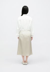 Άσπρο πουκάμισο με μακριά μανίκια και καλοσχηματισμένη εφαρμογή, σε συνδυασμό με μπεζ σατέν μίντι φούστα. Ομαλή υφή και μινιμαλιστικός σχεδιασμός χωρίς ορατά μοτίβα.