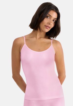 Woman with shoulder-length dark hair wearing a light pink sleeveless camisole top against a plain white background.