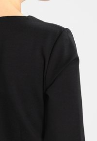 Mustat kankaatoppi, jossa on sileä pinta, pyöreä kaula-aukko ja jämäkät olkasaumat, esittelee minimalistista muotoilua.