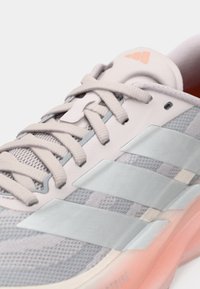 Svetlosivá športová obuv s vrchnou časťou z oka, textúrované šnúrky, výrazný dizajn troch pruhov v svetlomodrej farbe a priehľadné ružové akcenty na podrážke.