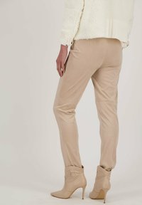 Beige fitted broeken met een gladde textuur, gecombineerd met lichtbruine hoge enkellaarsjes met een gevouwen ontwerp en een puntige neus.