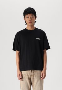 Sort bomulds T-shirt med løs pasform, rund halsudskæring og korte ærmer. Har hvidt varemærke logo på venstre brystområde.
