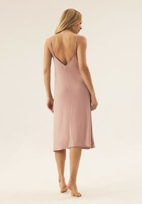 Różowa sukienka na ramiączkach w kolorze brudnego różu, z dekoltem w kształcie litery V na plecach, gładka w dotyku, długości do kolan, z delikatnym blaskiem i prostymi liniami.