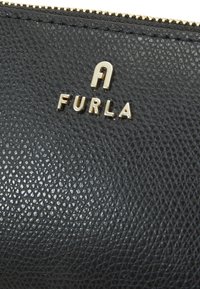 Svart lærpung med teksturert overflate, med en gullfarget "FURLA"-logo og metallglidelås. Sofistikert og elegant design.