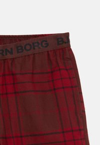 Röd och brun rutigt tyg med ett svart elastiskt midjeband som har delvis synlig text "BJORN BORG".