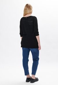Maglione nero a maglia con righe orizzontali, maniche lunghe e scollatura rotonda. Abbinato a jeans blu a gamba affusolata e scarpe nere spesse.