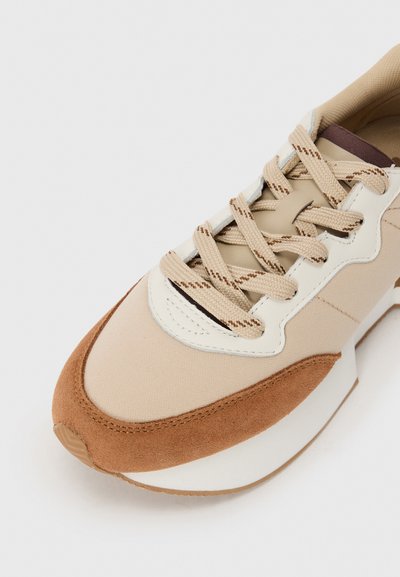 Beige sneaker with suede and fabric materials, cream accents, and textured beige laces. Slightly rounded toe and padded collar.