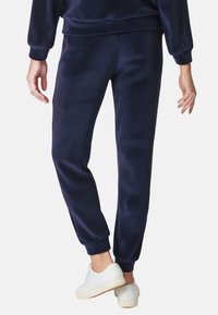 Marineblaue, weiche Jogginghosen mit elastischen Bündchen. Kombiniert mit weißen Sneakers, zeigen sie eine lockere Passform und eine glatte Textur.