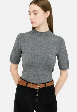 Maglione grigio a maniche corte in maglia con colletto alto, caratterizzato da un motivo testurizzato e sottili brillanti, abbinato a pantaloni neri a vita alta e una cintura marrone.
