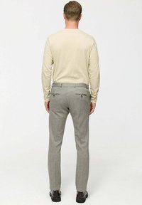 Lichtbeige langemouwshirt met aansluitende grijze broek met een subtiele textuur en twee achterzakken. Schoenen zijn zwart met een gladde afwerking.