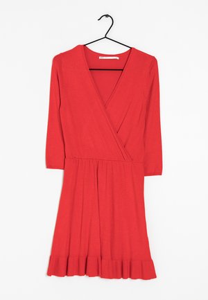 Vestido rojo envolvente con escote en V, mangas tres cuartos y dobladillo plisado. Hecho de una tela suave con una textura lisa. Cuelga de un gancho negro.