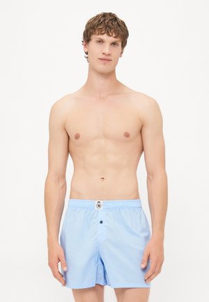 Helle blaue Badehosen aus weichem Stoff mit elastischem Bund, ausgestattet mit einem Frontknopfverschluss und einem kleinen Logopatch.