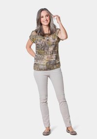 Korte mouwen, multiculturele top met abstracte patronen in aardetinten; gecombineerd met lichtbeige slim-fit broeken en grijze flats.