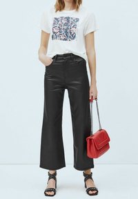 Svarta i läderliknande material med vida ben, vit grafisk t-shirt med blommönster, röd handväska och svarta sandaler med klack och remmar.