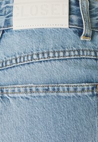 Jasnoniebieskie dżinsy z widocznym przeszyciem, tylną kieszenią, szlufką na pasek i białą skórzaną metką z wytłoczonym napisem "CLOSED."