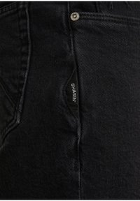 Mustat farkut, joissa on sivutasku ja "CHASIN'" -merkki, hopeiset napit ja sileä pinta, jossa on vähäisiä ompeluyksityiskohtia.