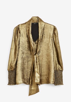 Blouse métallisée dorée à manches longues avec un col en V profond, un détail noué à l'avant, des épaules bouffantes et des poignets froncés.