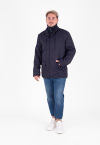 Giacca esterna blu navy realizzata in tessuto morbido, con colletto alto, bottoni a scatto, due tasche frontali, vestibilità slim e coulisse regolabili.