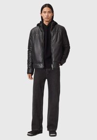 Sort læderjakke med lynlås, båret over en sort hættebluse. Sammen med mørke lige ben jeans og sorte støvler. Enkel design.