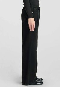 Zwarte brede denim jeans met riemlussen en voorzakken. De stof heeft een matte afwerking en beschikt over zilveren hardware accenten.