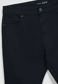 Granatowe dżinsy o gładkiej fakturze, pięć kieszeni i metalowe zapięcie. Zawierają detale przeszycia wzdłuż szwów.