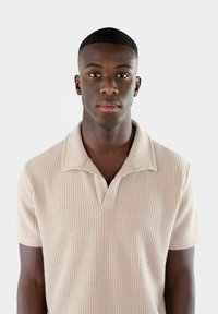 Beige kortärmad polo shirt med en strukturerad, ribbad mönster och en notched krage. Tyget verkar mjukt och lätt.