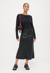 Fekete, hosszú ujjú felső, amelyet egy magas derekú fekete bőrszoknyával viselnek. Vastag fekete cipővel kombinálva, lila részletekkel, és egy bordó táskával.