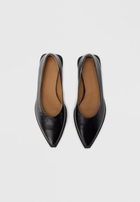 Chaussures plates en cuir noir avec bout pointu et talon ouvert. Texture lisse avec une semelle intérieure marron arborant le nom de la marque en relief.