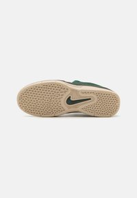 Sapatilhas verde em camurça com uma sola de borracha texturizada bege, apresentando um padrão de aderência e o logótipo Nike em verde escuro.