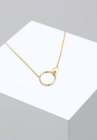 Gold circular pendant necklace on a fine chain, featuring a smooth large ring and a smaller disc detail, with a polished surface.