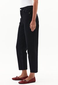 Svarta högmidjade jeans med raka ben, med knappgylf och kopparnitar, i kombination med röda ballerina skor.