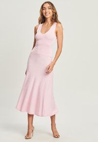 Abito maxi smanicato di un rosa chiaro, a coste, con un busto aderente e una gonna svasata. Texture liscia, lunghezza al ginocchio, design minimalista.