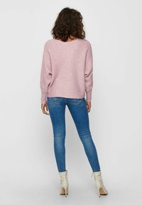 Un pull en tricot rose avec une coupe décontractée, associé à un jean skinny bleu. La tenue est complétée par des bottines blanches.
