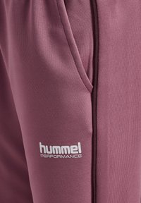 Præstations-joggers i en lys mauve farve, lavet af glat stof. Har en sidelomme og et hvidt logo på venstre lår.