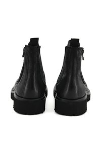 Stivali alla caviglia in pelle nera con una finitura liscia, pannelli laterali elastici e chiusure con zip. Suole spesse in gomma con un motivo a gobbato.