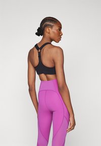 Schwarzer Sport-BH mit verstellbaren Trägern und Rückenausschnitt, kombiniert mit hoch taillierten rosa Leggings mit Nahtdetails.