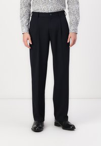 Pantaloni eleganți bleumarin, cu pliuri, dintr-un material neted. Au curea de prindere și închidere cu nasture, asortați cu pantofi negri.