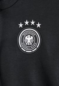 Tela negra con un emblema circular en blanco del Deutscher Fussball-Bund que presenta un águila y cuatro estrellas bordadas encima.