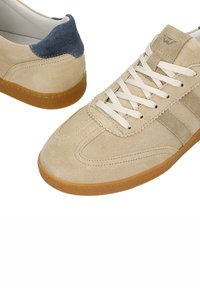 Baskets en daim beige avec semelles en gomme, lacets blancs et languette de talon bleu foncé, vues de côté et de dessus sur fond blanc.